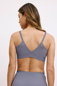 On a white studio backdrop, a back view shows the Bliss Triangle Bralette in Steel, focusing on the adjustable straps, V-shaped back, and wide underband designed for comfortable, wireless support.