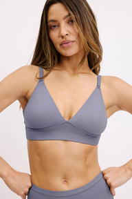 On a clean white backdrop, a model wears the Bliss Triangle Bralette in Steel, shown in a close-up that highlights the deep V neckline, smooth microfiber fabric, and thin adjustable straps for soft, wireless comfort. sizing: Darion wears size Small