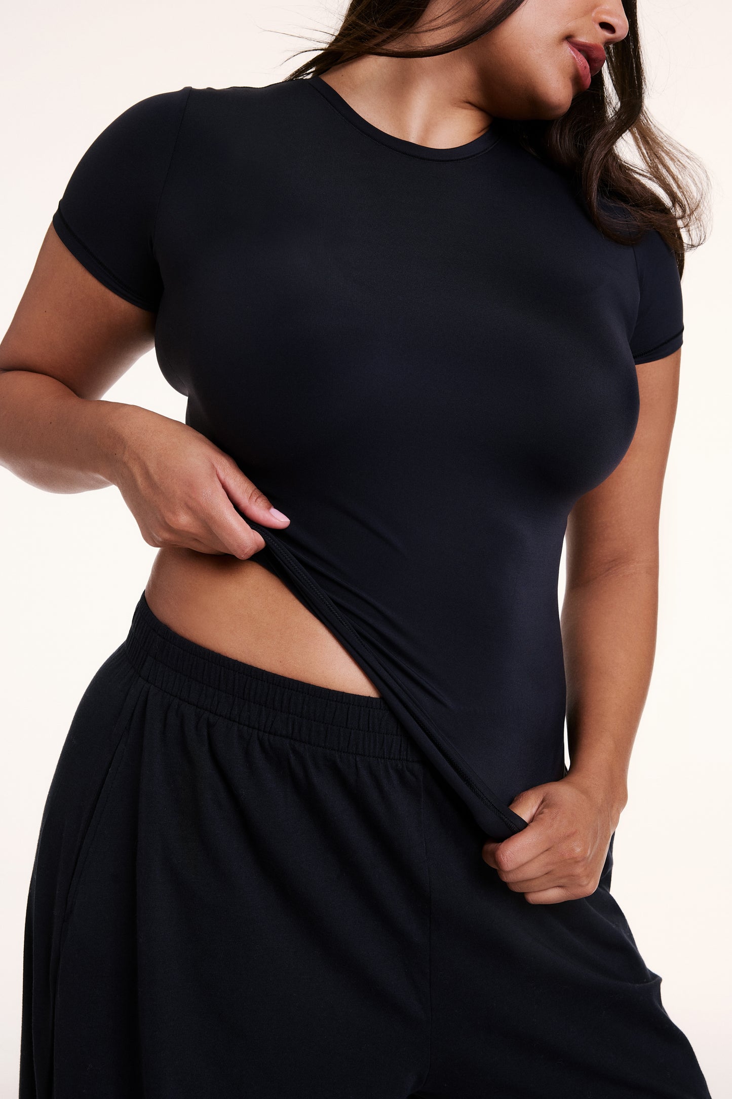 In a close-up studio shot, Alana wears the Bliss Apparel T-Shirt in Black, highlighting the smooth, lightweight fabric and close fit across the chest and torso. sizing: Alana wears size Large