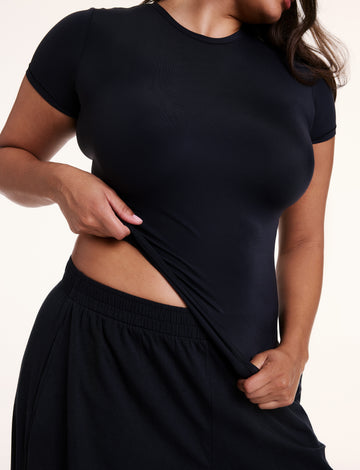 In a close-up studio shot, Alana wears the Bliss Apparel T-Shirt in Black, highlighting the smooth, lightweight fabric and close fit across the chest and torso. sizing: Alana wears size Large