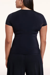 In a studio setting, Alana is shown from the back wearing the Bliss Apparel T-Shirt in Black, featuring short sleeves and a smooth, second-skin fit.