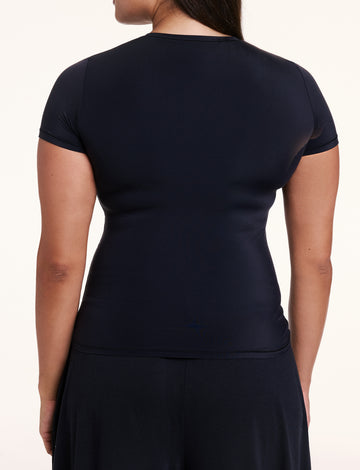 In a studio setting, Alana is shown from the back wearing the Bliss Apparel T-Shirt in Black, featuring short sleeves and a smooth, second-skin fit.