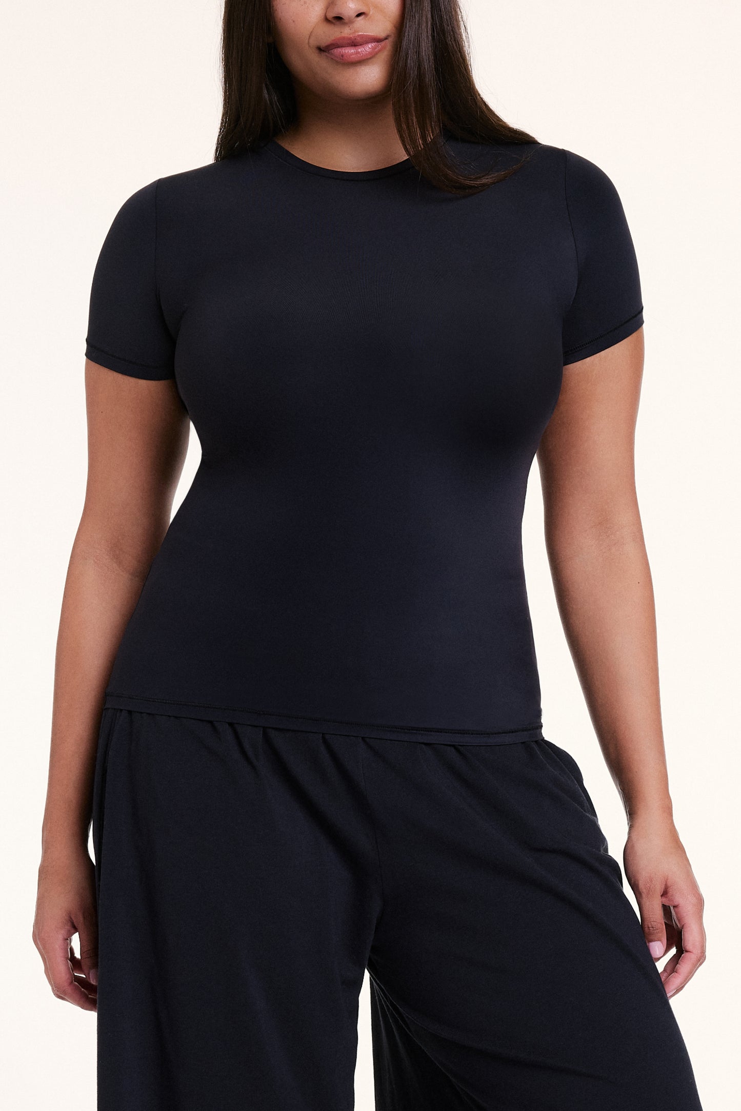 In a studio setting, Alana wears the Bliss Apparel T-Shirt in Black with matching pants, highlighting the crew neckline, short sleeves, and soft, body-hugging fabric.