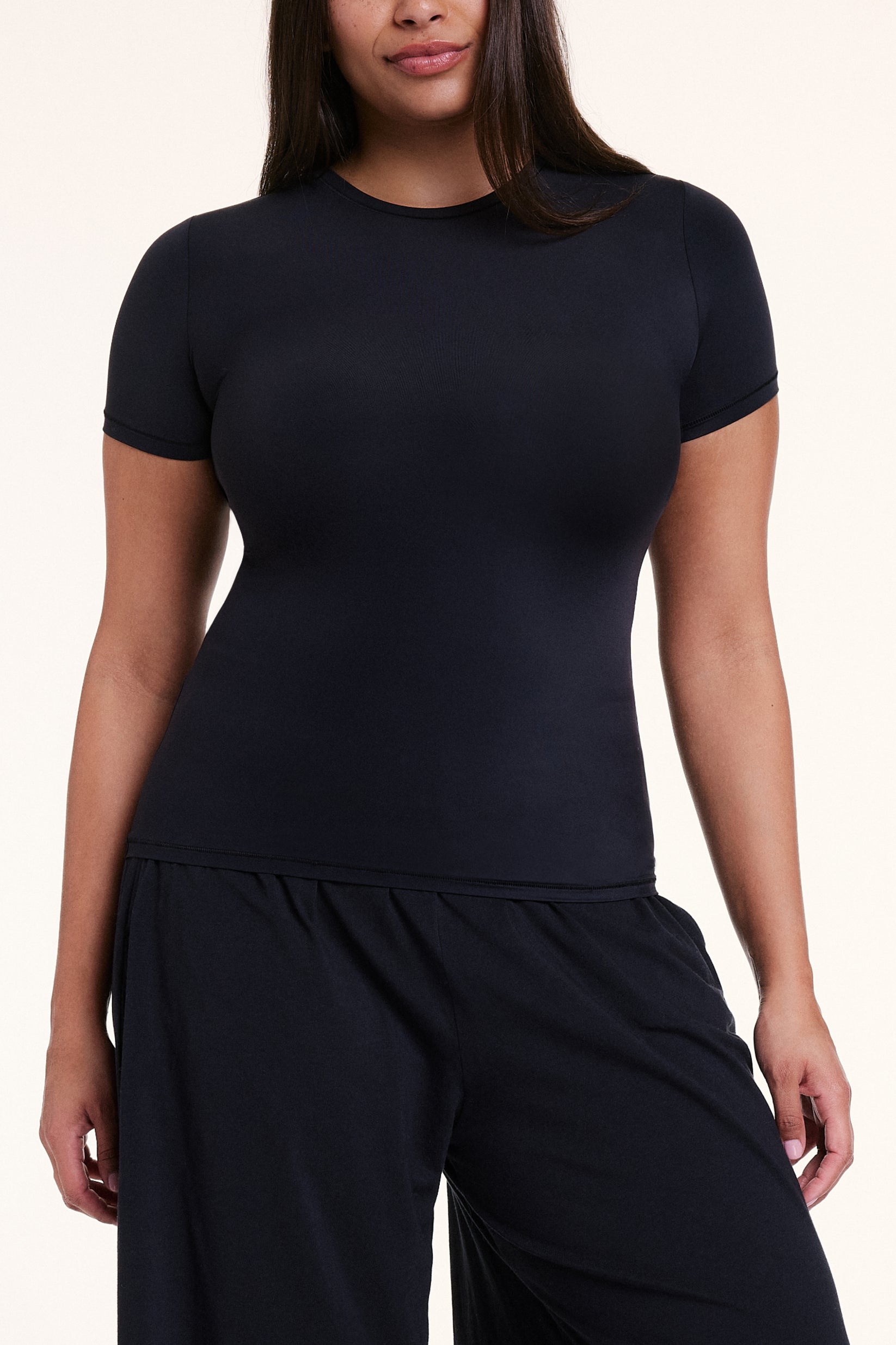 In a studio setting, Alana wears the Bliss Apparel T-Shirt in Black with matching pants, highlighting the crew neckline, short sleeves, and soft, body-hugging fabric.