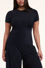 In a studio setting, Alana wears the Bliss Apparel T-Shirt in Black with matching pants, highlighting the crew neckline, short sleeves, and soft, body-hugging fabric.