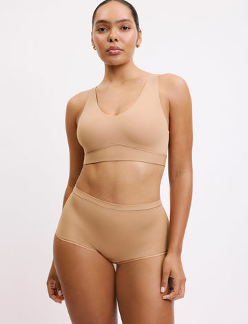 On a white studio backdrop, Amber wears the Bliss Bralette and Bliss Boyshort in Beige, standing facing forward. The bralette features a scoop neckline, wide straps, and a smooth underband, paired with mid-rise boyshorts in soft, lightweight fabric.