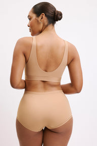 On a white studio backdrop, Amber wears the Bliss Bralette and Bliss Boyshort in Beige, shown from the back. The bralette features a scoop back and wide straps, paired with full-coverage boyshorts and a smooth waistband.