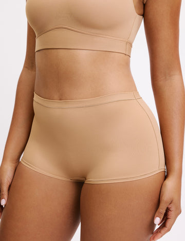 On a white studio backdrop, Amber wears the Bliss Bralette and Bliss Boyshort in Beige, shown in a close-up. The bralette features a scoop neckline and smooth underband, paired with mid-rise boyshorts in soft, lightweight fabric. sizing: Amber wears size Large