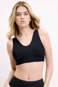 On a white studio backdrop, Megan wears the Bliss Bralette in Black, shown from the front. The scoop neckline, wide straps, and smooth microfiber fabric are visible for an everyday, wireless feel. sizing: Megan wears size Small