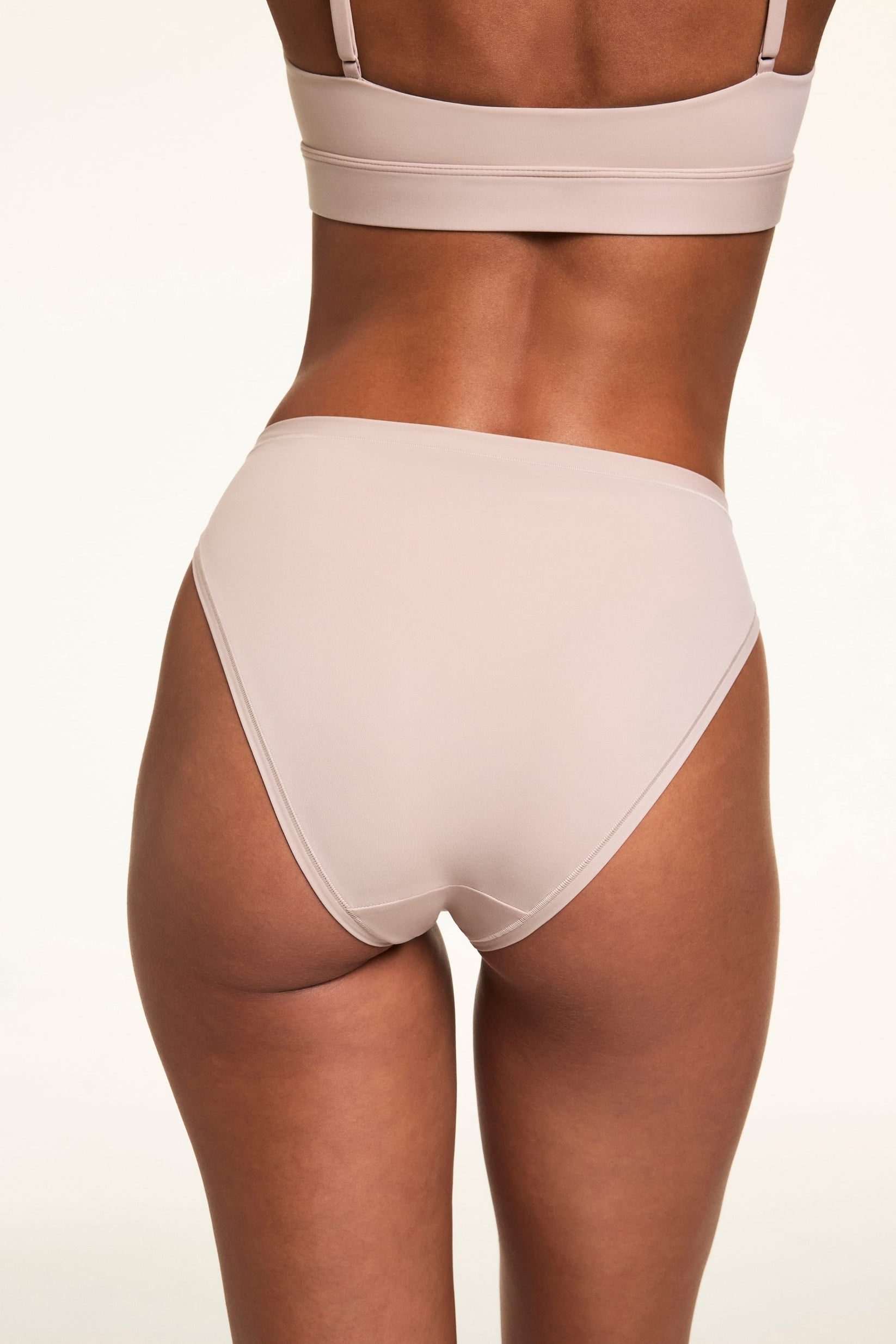 From the back, Linni wears the Bliss French Cut Brief in Pebble, highlighting the smooth microfiber fabric and moderate back coverage.
