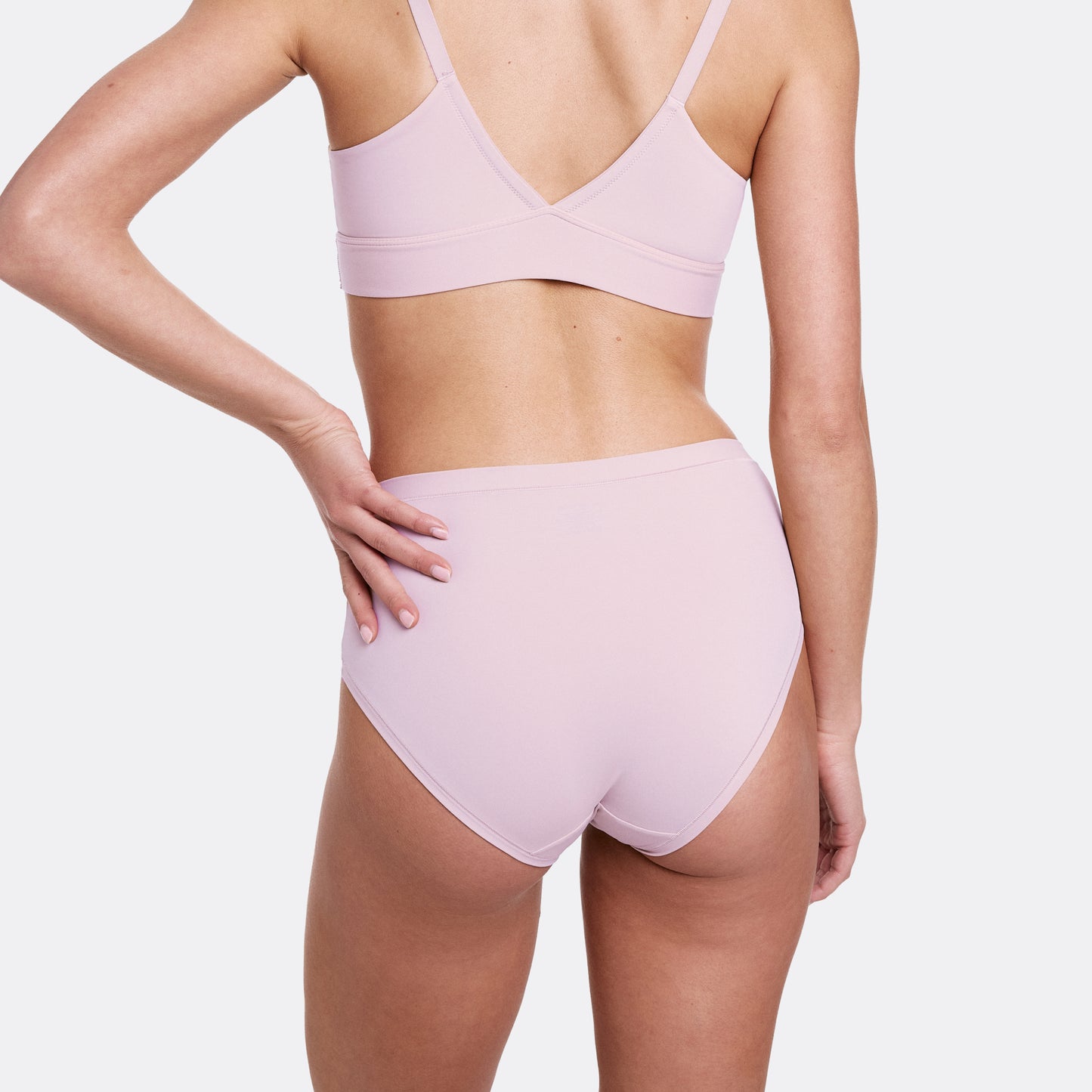 In a studio setting with a neutral backdrop, Gianna wears the Bliss Triangle Bralette and Bliss Highwaist Brief in Retro Lilac, shown from the back. The high-rise underwear provides full coverage with ultra-soft microfiber fabric and a smooth, elastic-free finish.