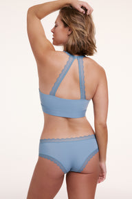 In a white studio setting, Sonnie wears the Bliss Lace Cheeky in Poolside with the Bliss Bralette, shown from the back featuring lace racerback straps, a wide underband, and cheeky coverage with scalloped lace trim.