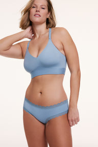 In a white studio setting, Sonnie wears the Bliss Bralette and Bliss Lace Cheeky in Poolside, featuring a V-neckline, adjustable straps, and a wireless band, paired with a low-rise cheeky silhouette with scalloped lace trim.