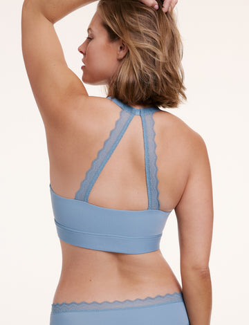 In a studio setting with a neutral backdrop, Sonnie wears the Bliss Lace Halterneck Bralette and matching underwear in Poolside blue, shown from the back. The bralette features a halterneck silhouette with lace racerback detailing, paired with smooth microfiber fabric and lace-trimmed edges. sizing: Sonnie wears size Large