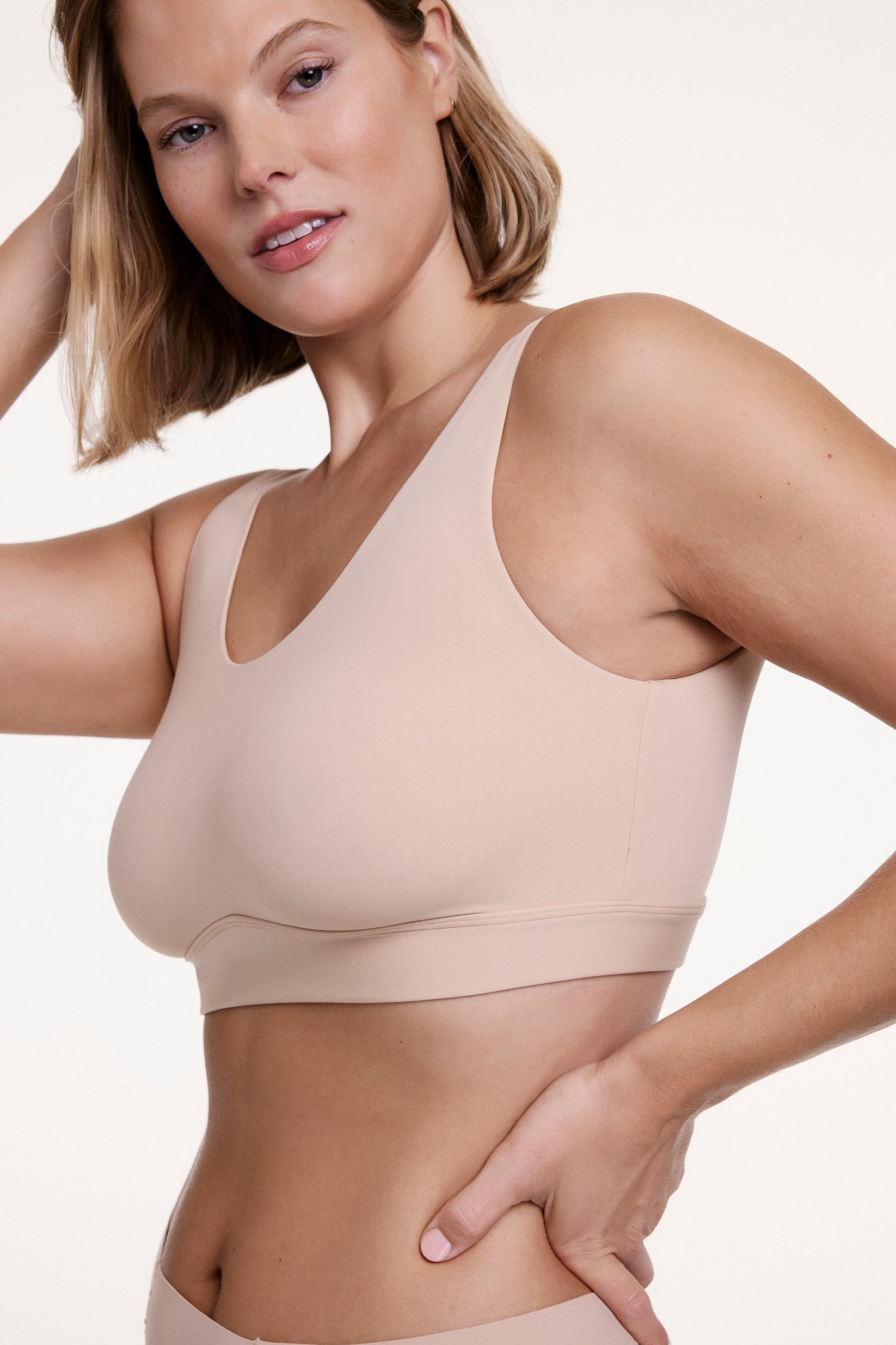In a studio setting, Sonnie wears the Bliss Scoop Bralette in Beige, highlighting the scoop neckline, smoothing sides, and ultra-soft microfiber fabric for comfortable, everyday support.