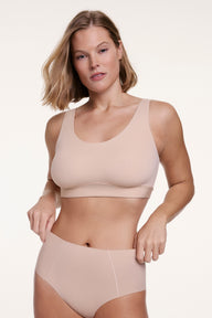 In a studio setting, Sonnie wears the Bliss Scoop Bralette in Beige with matching underwear, featuring a scoop neckline, wireless lift, and soft microfiber fabric for lightweight comfort.