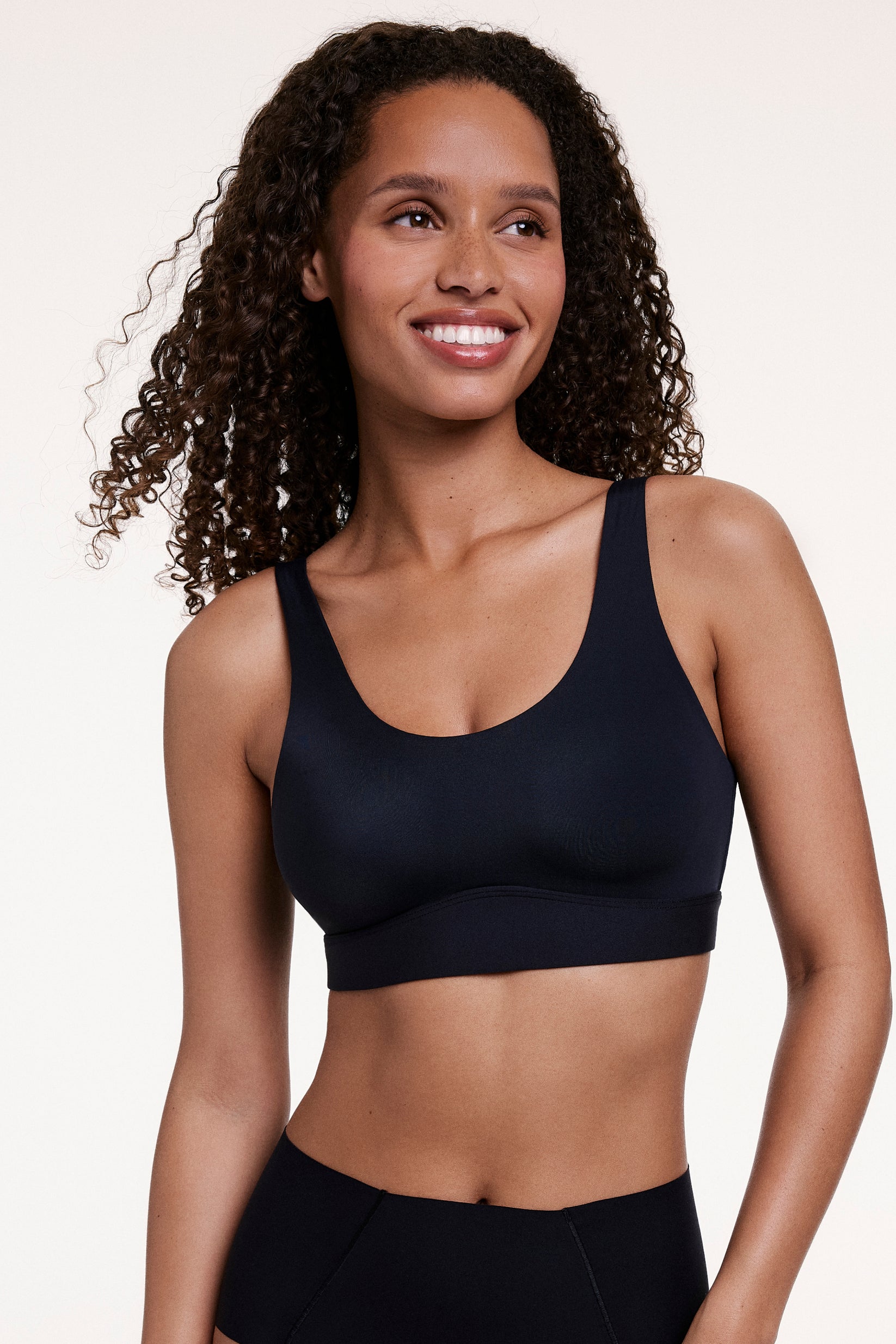 In a studio setting, Courtney wears the Bliss Scoop Bralette in Black, featuring a scoop neckline, wireless lift, and soft microfiber fabric for lightweight, everyday comfort. sizing: Courtney wears size Small