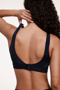 In a studio setting, Courtney wears the Bliss Scoop Bralette in Black, shown from the back with thin adjustable straps and a hook-and-eye closure for a customizable, comfortable fit.