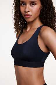 In a studio setting, Courtney wears the Bliss Scoop Bralette in Black, featuring a scoop neckline, smoothing sides, and ultra-soft microfiber fabric for lightweight, comfortable support.