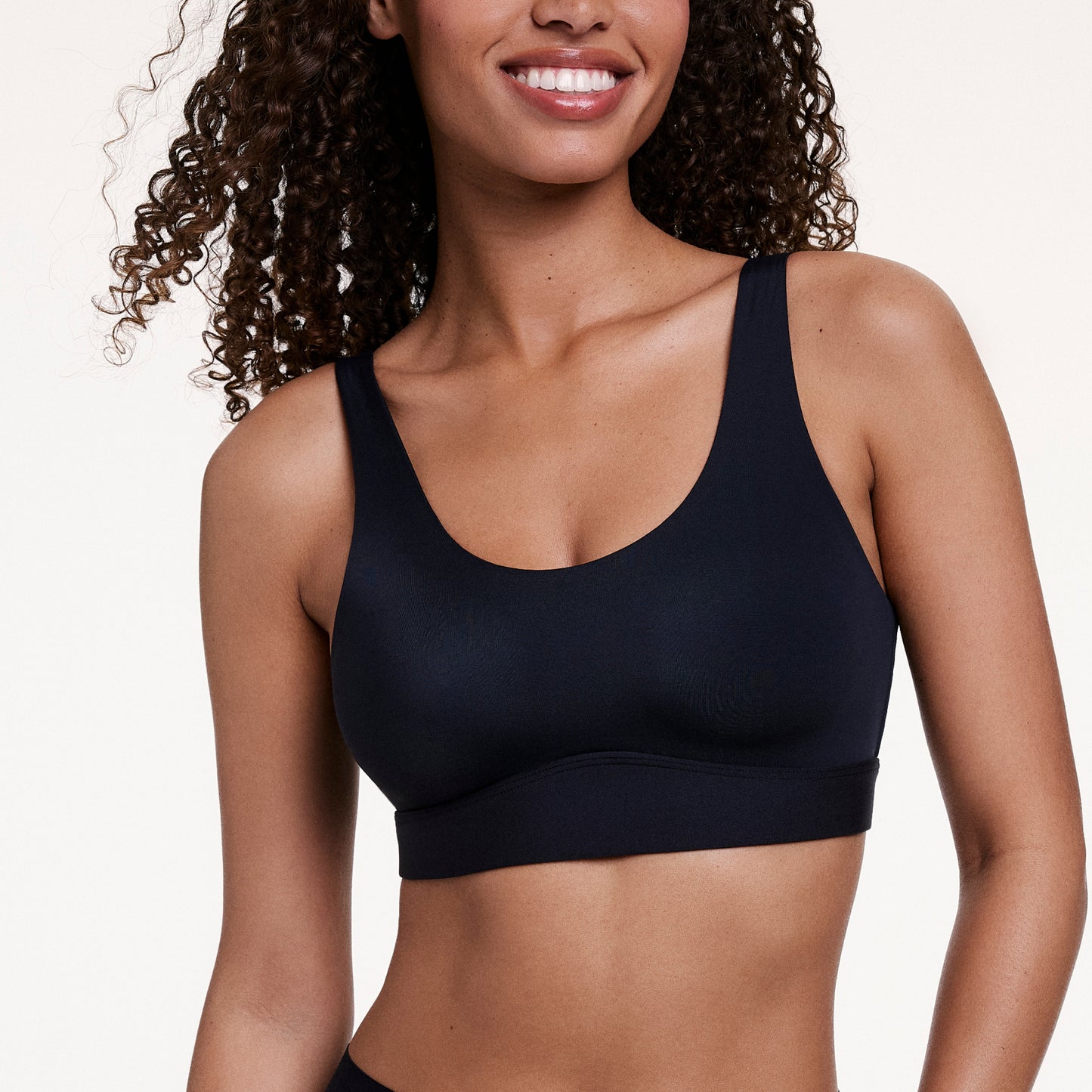 In a studio setting, Courtney wears the Bliss Scoop Bralette in Black, highlighting the scoop neckline, smoothing sides, and ultra-soft microfiber fabric for comfortable support.