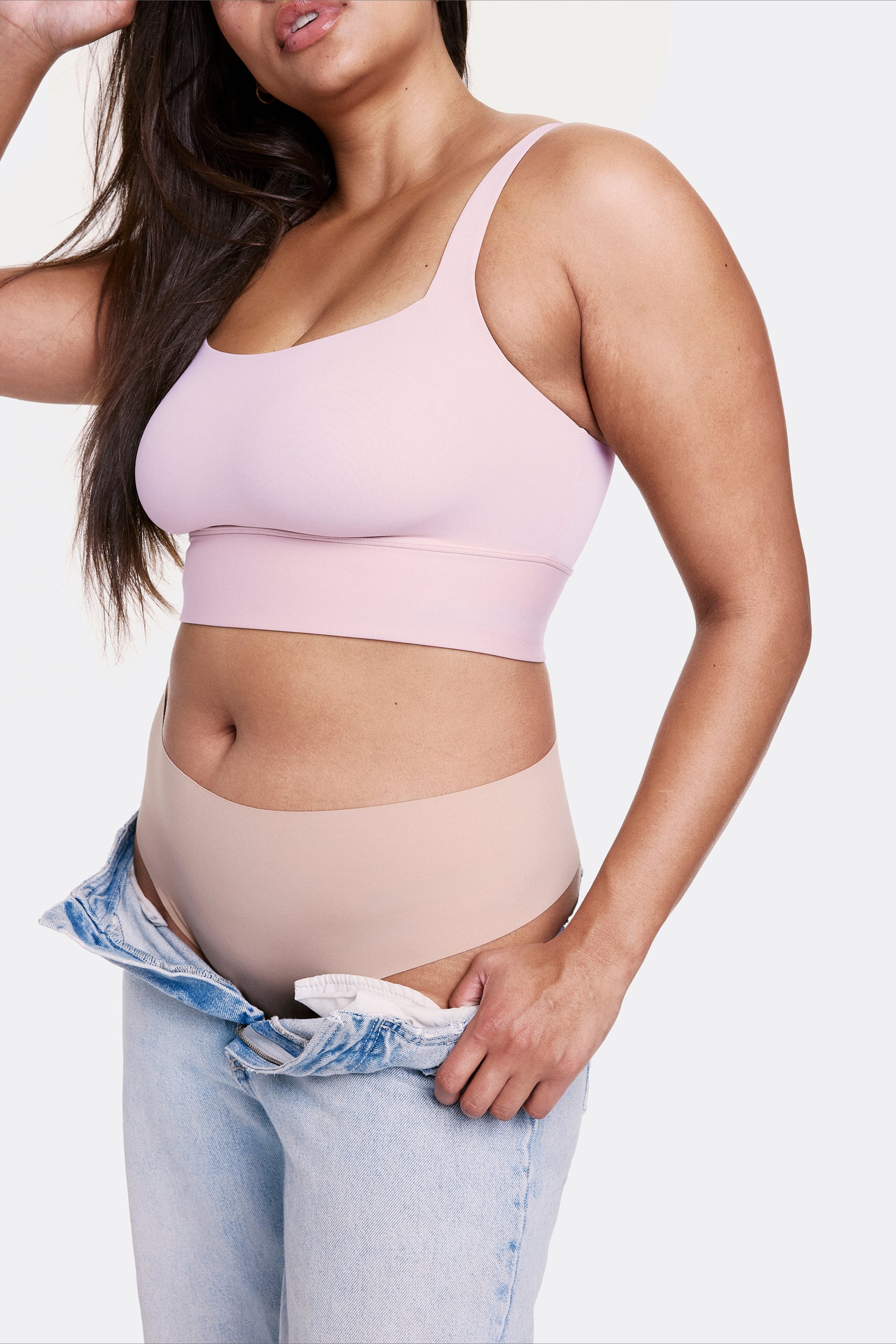 In a studio setting with a light gray backdrop, Alana wears the Bliss Square Neck Bralette in Retro Lilac with matching underwear and relaxed denim, highlighting the square neckline and longline silhouette. The bralette features thin adjustable straps and a soft wireless band, made from smooth microfiber fabric for comfortable support.
