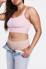 In a studio setting with a light gray backdrop, Alana wears the Bliss Square Neck Bralette in Retro Lilac with matching underwear and relaxed denim, highlighting the square neckline and longline silhouette. The bralette features thin adjustable straps and a soft wireless band, made from smooth microfiber fabric for comfortable support.