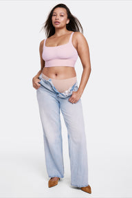 In a studio setting with a light gray backdrop, Alana wears the Bliss Square Neck Bralette in Retro Lilac with matching underwear and relaxed denim, shown full length to highlight the square neckline and longline design. Thin adjustable straps and a soft wireless band provide a comfortable, flexible fit.