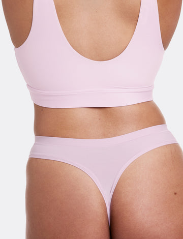 In a studio setting with a neutral backdrop, Alana wears the Bliss Scoop Bralette and Bliss Thong in Retro Lilac, shown from the back. The thong features minimal back coverage, ultra-soft microfiber fabric, and an elastic-free design for a smooth, comfortable feel.