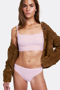 In a studio setting with a neutral backdrop, Gianna wears the Bliss Square Neck Bralette and Bliss Thong in Retro Lilac, layered under an open brown jacket. The bralette features a square neckline, wireless band for support, and ultra-soft microfiber fabric. sizing: Gianna wears size Small
