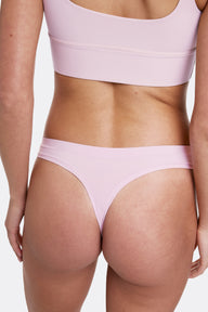 In a studio setting with a neutral backdrop, Gianna wears the Bliss Thong in Retro Lilac, shown from the back. The thong features minimal back coverage, ultra-soft microfiber fabric, and an elastic-free design for a smooth, comfortable feel.