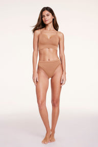 Full-body view of Linni wearing the Cloud Cotton Triangle Bralette and Cloud Cotton French Cut underwear in Dune, highlighting the soft V-neckline, adjustable straps, and high-cut underwear silhouette.