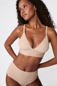 Three-quarter angle shot of model looking to the side, showcasing the smooth triangle cup silhouette and adjustable straps of the Harper Wilde Bliss Triangle bralette in beige.