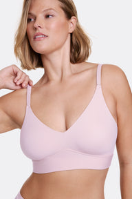 In a studio setting with a neutral backdrop, Sonnie wears the Bliss Triangle Bralette in Retro Lilac, shown in a close-up view. The bralette features a deep V neckline, wireless band for lift, and ultra-soft microfiber fabric. She gently adjusts the front strap, highlighting the front-adjusting straps for a customizable fit. sizing: Sonnie wears size Large