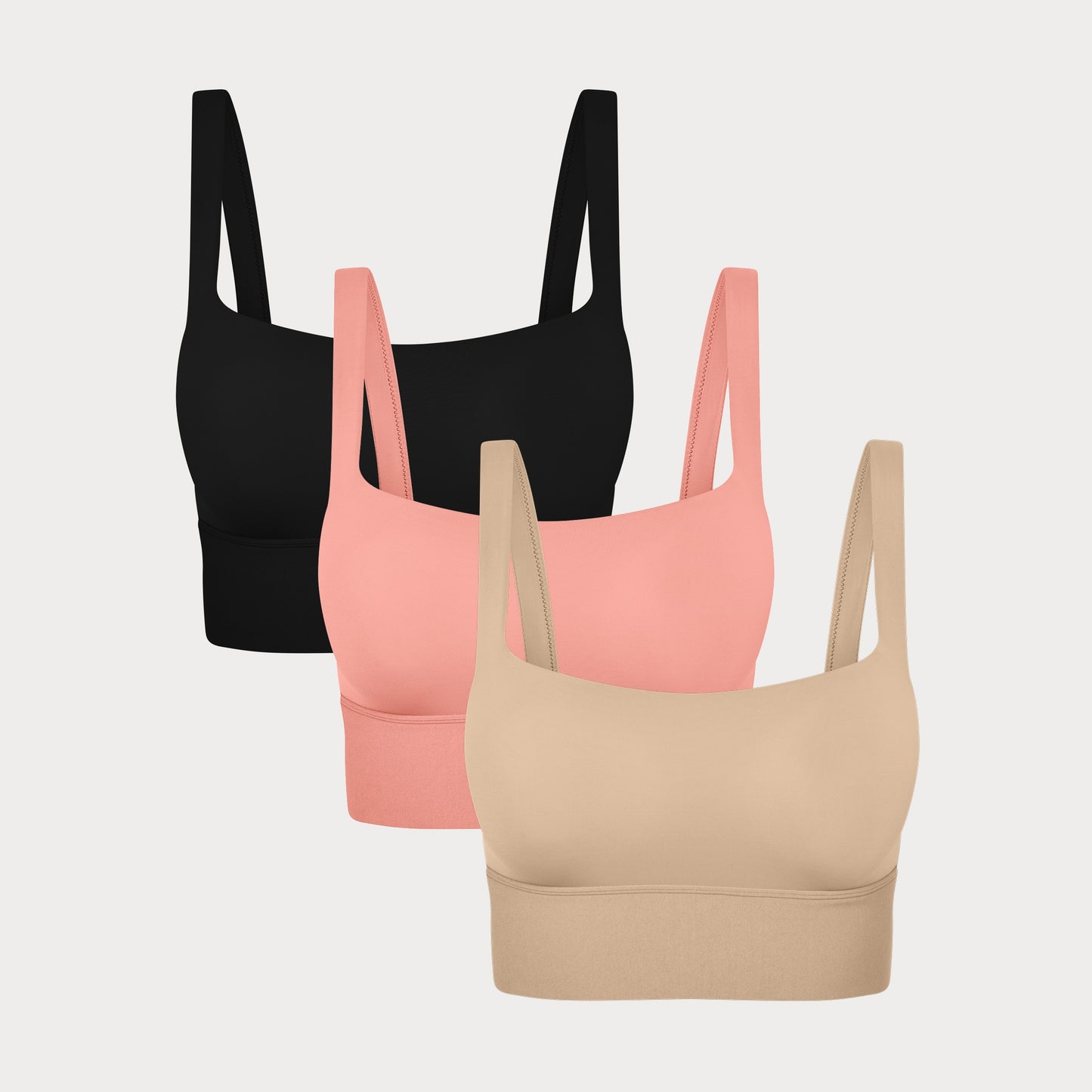 Three Bliss Squareneck Bralettes in Black, Cabana, and Beige displayed on a light grey background, showing the wide square neckline and thick shoulder straps.