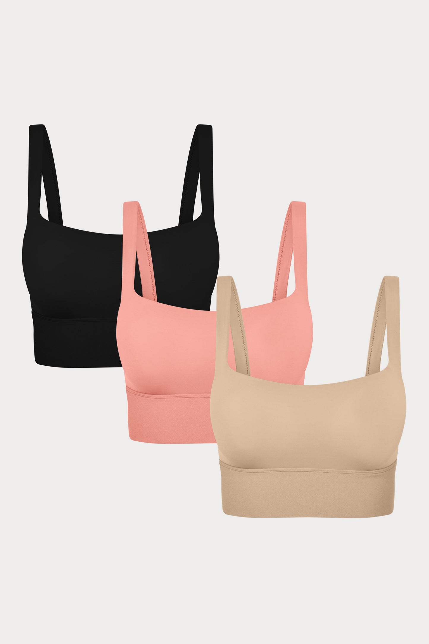 Three Bliss Squareneck Bralettes in Black, Cabana, and Beige displayed on a light grey background, showing the wide square neckline and thick shoulder straps.
