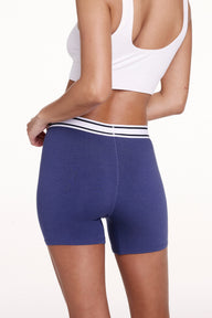 On a white studio backdrop, Courtney wears the Cloud Cotton Boxer Brief in Desert Shadow, shown from the back. The boxer brief offers full back coverage with a mid-rise fit and soft cotton modal fabric, finished with a striped elastic waistband.