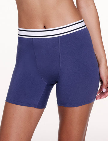 On a white studio backdrop, Courtney wears the Cloud Cotton Boxer Brief in Desert Shadow, shown in a close-up. The boxer brief features a mid-rise waistband, longer leg length, and smooth, stretchy cotton modal fabric. sizing: Courtney wears size Small