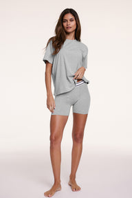 In a white studio setting, Linni wears the Cloud Cotton Boxer Brief in Heather Grey with a matching tee, standing relaxed. The boxer brief features a mid-rise fit, longer leg coverage, and soft cotton modal fabric with a striped elastic waistband.