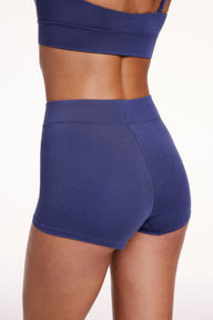 On a white studio backdrop, Linni wears the Cloud Cotton Boyshort in Desert Shadow, shown from the back. The boyshort features a high-rise waistband and full coverage in soft cotton modal fabric.