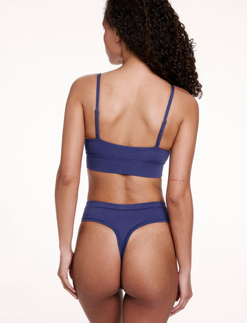 On a white studio backdrop, Courtney wears the Cloud Cotton High Waist Thong in Desert Shadow, shown from the back. The thong features a high-rise waistband and minimal back coverage in soft cotton modal fabric.