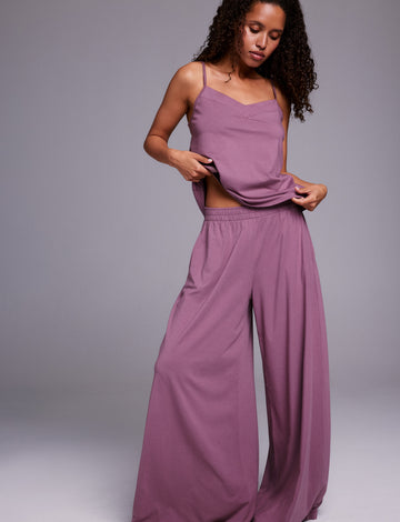 In a studio setting, Courtney wears a matching lounge set in Mirage, lifting the hem of a soft V-neck tank with thin straps to show the lightweight, breathable fabric and relaxed fit of the wide-leg pants.