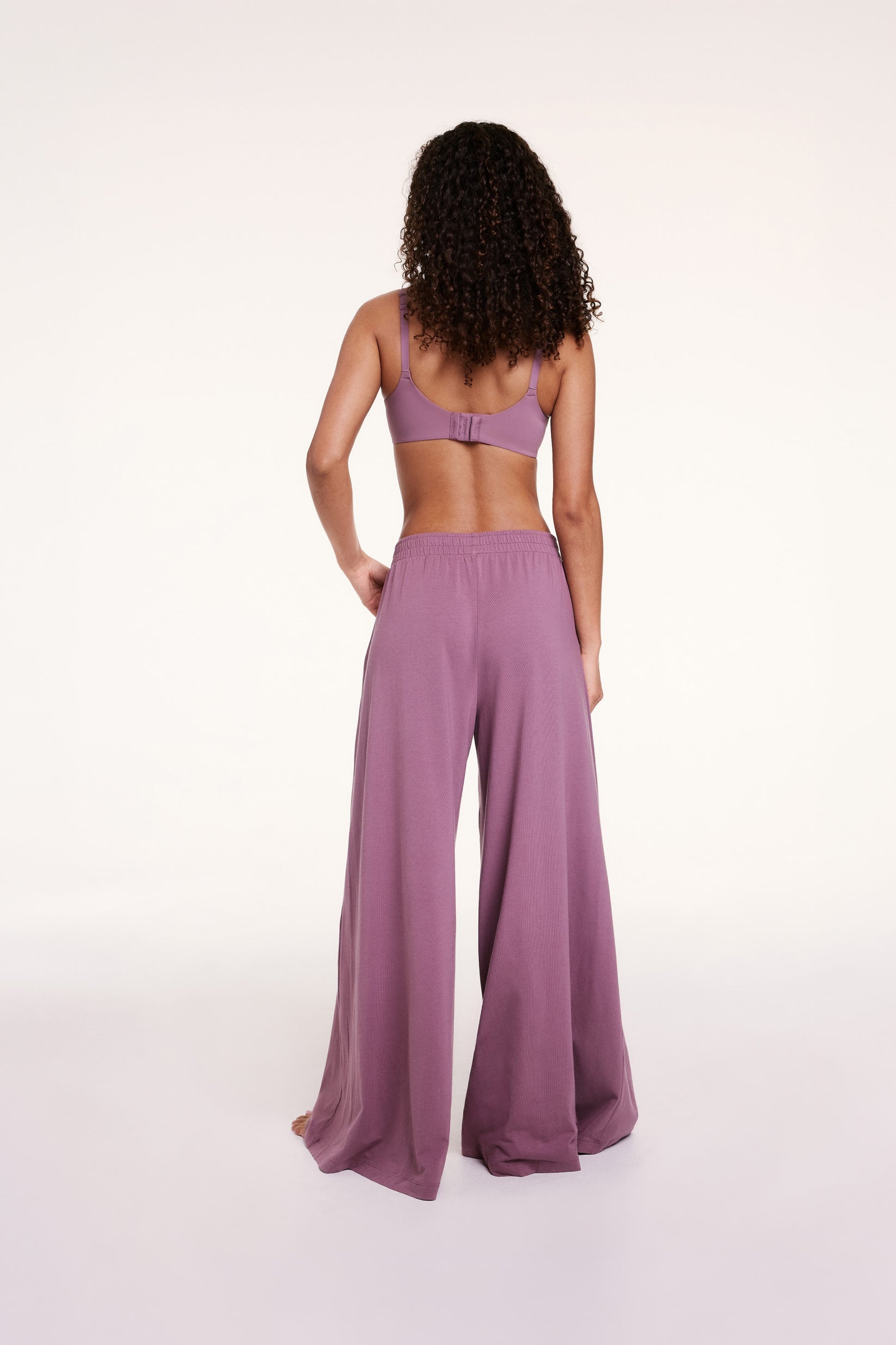 In a studio setting, Courtney wears Cloud Cotton pants in Mirage, shown from the back with an elastic waistband and a relaxed, wide-leg fit in soft, drapey fabric.