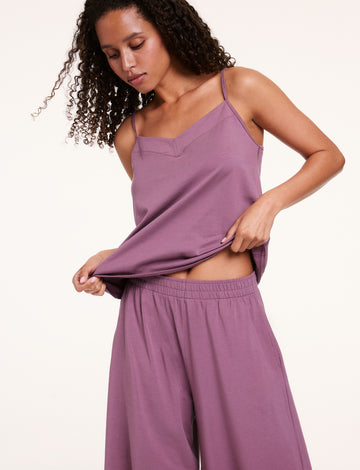 In a studio setting, Courtney wears a Cloud Cotton tank and pants in Mirage, lifting the hem to show the lightweight, breathable fabric and relaxed fit.