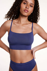 On a white studio backdrop, Courtney wears the Cloud Cotton Thin Strap Bralette in Desert Shadow with matching underwear, hands on hips. The bralette features a square neckline, thin adjustable straps, and a supportive longline band. sizing: Courtney wears size Small