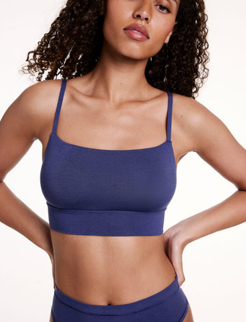 On a white studio backdrop, Courtney wears the Cloud Cotton Thin Strap Bralette in Desert Shadow with matching underwear, hands on hips. The bralette features a square neckline, thin adjustable straps, and a supportive longline band. sizing: Courtney wears size Small