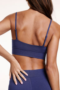 On a white studio backdrop, Linni wears the Cloud Cotton Triangle Bralette in Desert Shadow, shown from the back. The bralette features thin adjustable straps and a soft longline band.