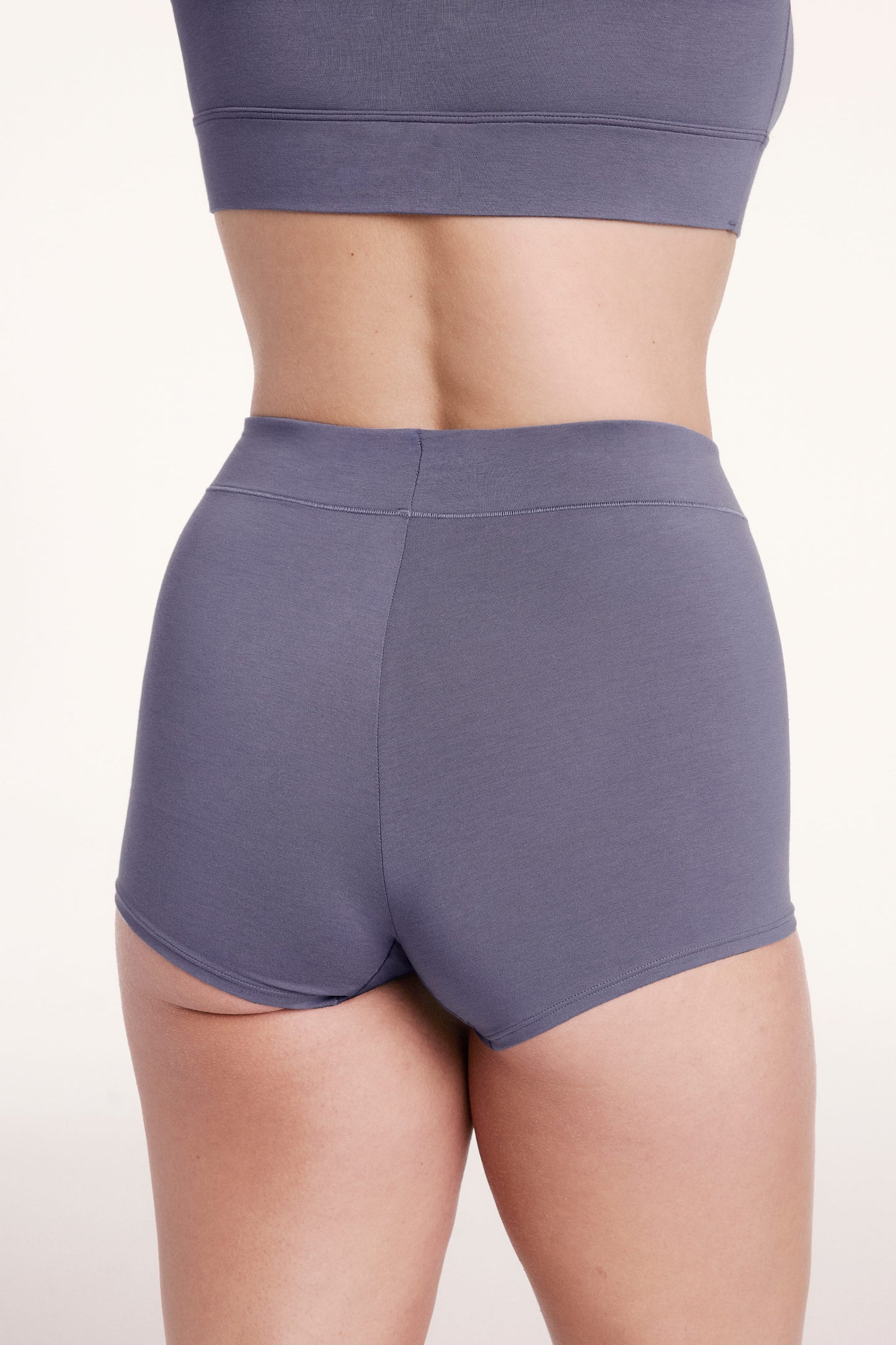 On a white studio backdrop, Sonnie wears the Cloud Cotton Boyshort in Slate, shown from the back with full coverage and a soft, stay-put waistband.