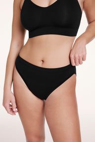 On a white studio backdrop, Sonnie wears the Cloud Cotton French Cut Brief in Black, shown in a front close-up highlighting the high-rise waist, French cut leg, and soft cotton modal fabric. sizing: Sonnie wears size Large