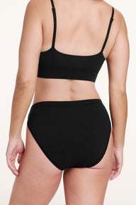 On a white studio backdrop, Sonnie wears the Cloud Cotton French Cut Brief in Black, shown from the back to highlight the mid- to full-coverage fit and smooth, stretchy fabric.