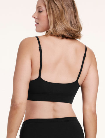 On a white studio backdrop, Sonnie wears the Cloud Cotton Triangle Bralette in Black, shown from the back with adjustable straps and a smooth, flexible band.
